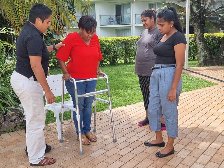 A mentor is standing next to a person using a learning frame, whilst explaining to two learners how to use the frame.
