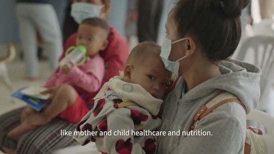 A mother wearing a mask holds her infant in a medical facility